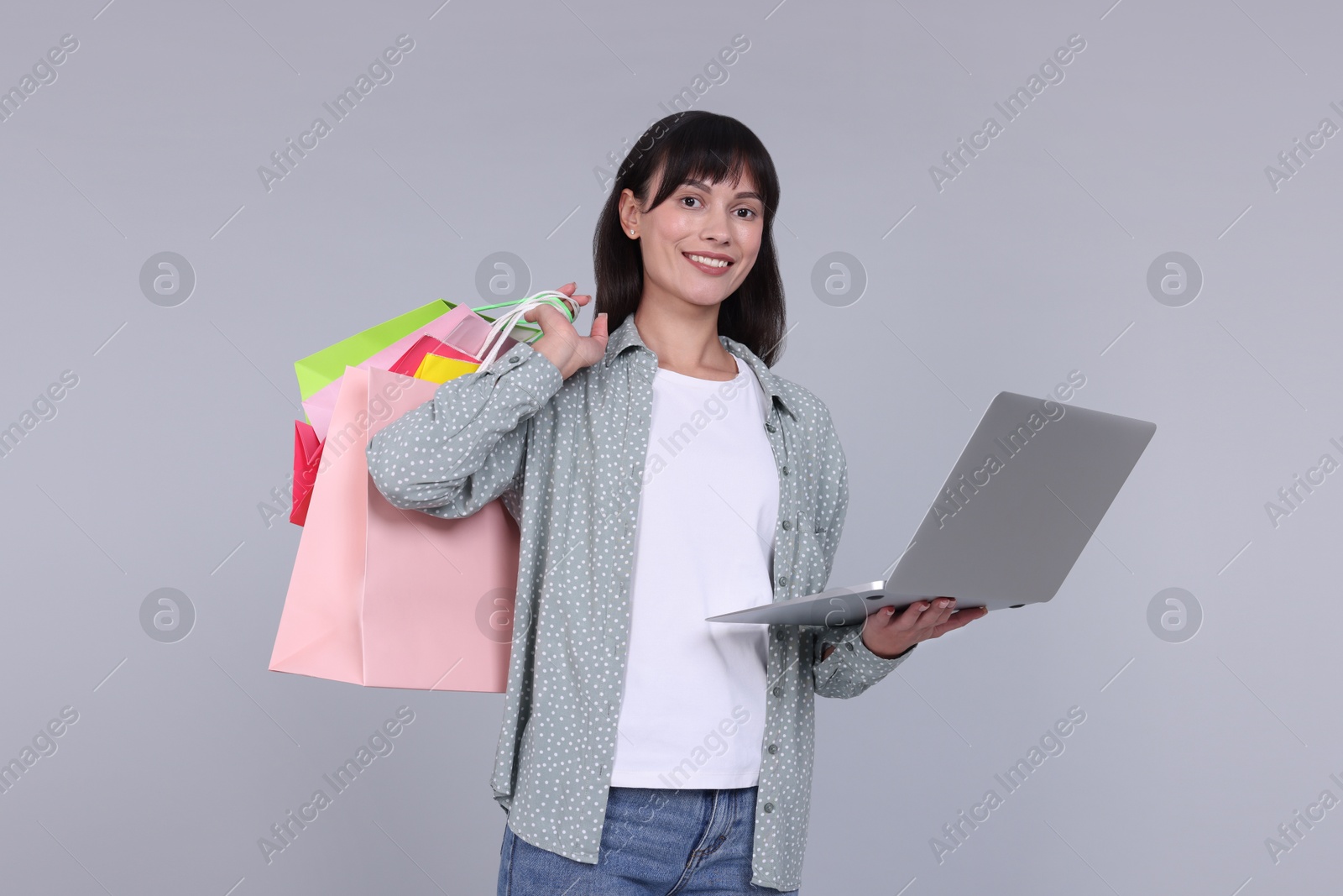 Photo of Internet shopping. Happy woman with laptop and colorful bags on grey background