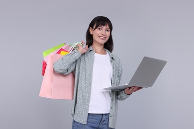 Photo of Internet shopping. Happy woman with laptop and colorful bags on grey background