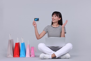 Photo of Internet shopping. Happy woman with credit card, laptop and colorful bags on grey background