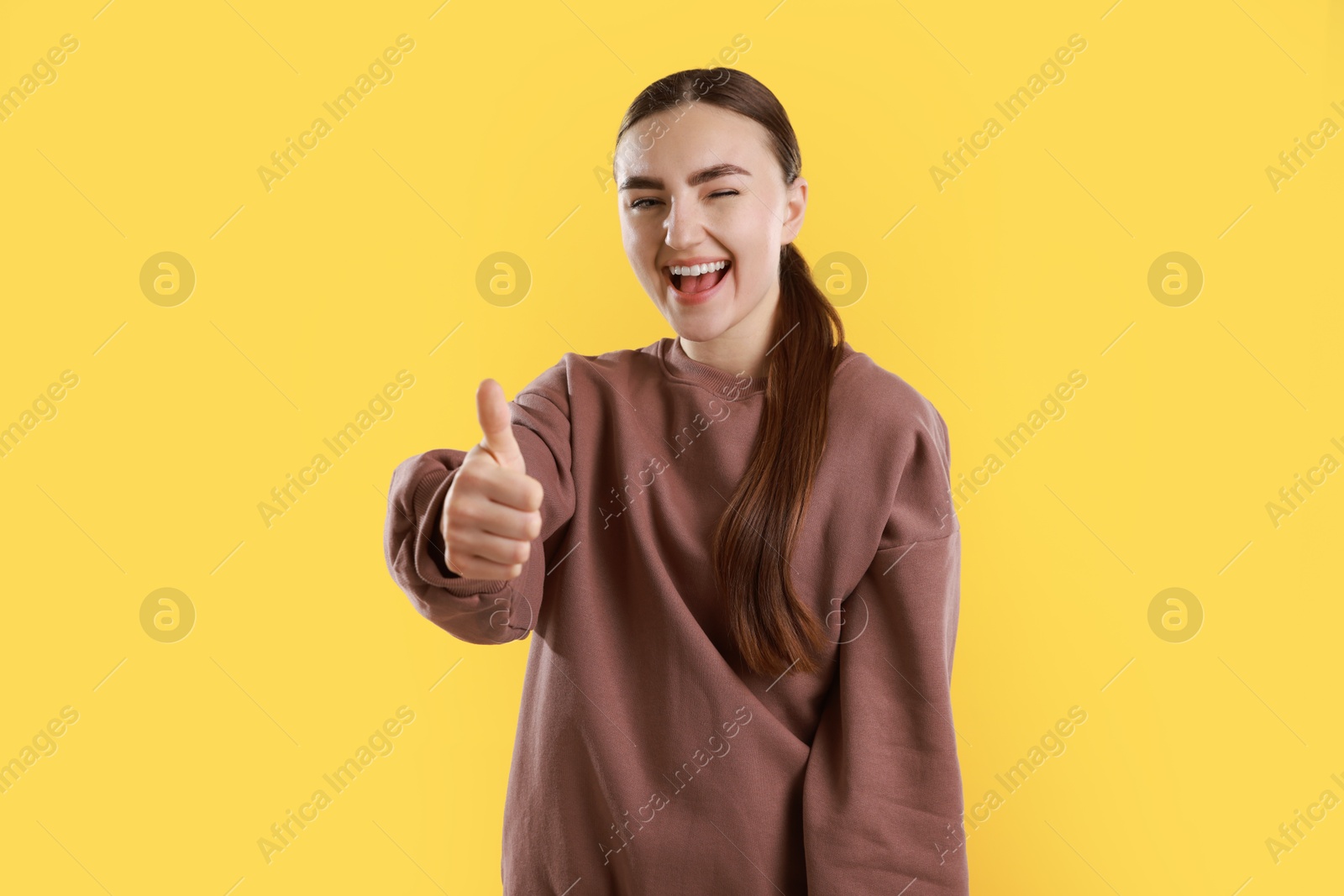 Photo of Happy woman showing thumbs up on yellow background. Like gesture