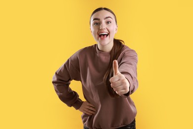 Photo of Happy woman showing thumbs up on yellow background. Like gesture