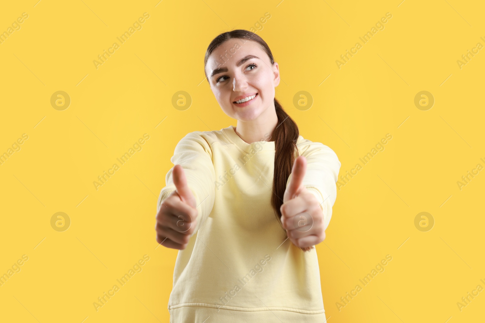 Photo of Happy woman showing thumbs up on yellow background. Like gesture