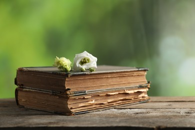 Photo of Books and beautiful flowers on wooden table against blurred green background, closeup