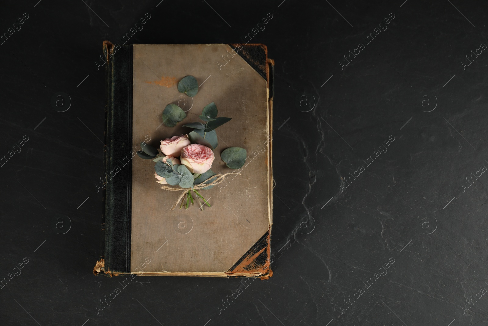 Photo of Old book, beautiful flowers and eucalyptus branches on dark textured table, top view. Space for text