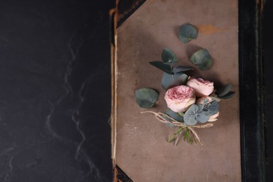 Photo of Old book, beautiful flowers and eucalyptus branches on dark textured table, top view. Space for text