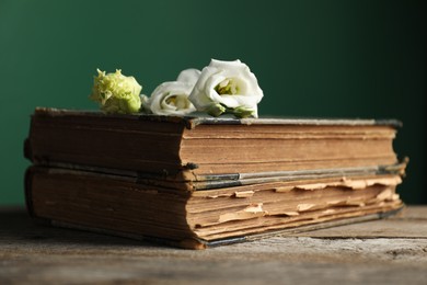 Books and beautiful flowers on wooden table against green background, closeup