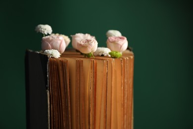 Photo of Book with beautiful flowers against green background, closeup