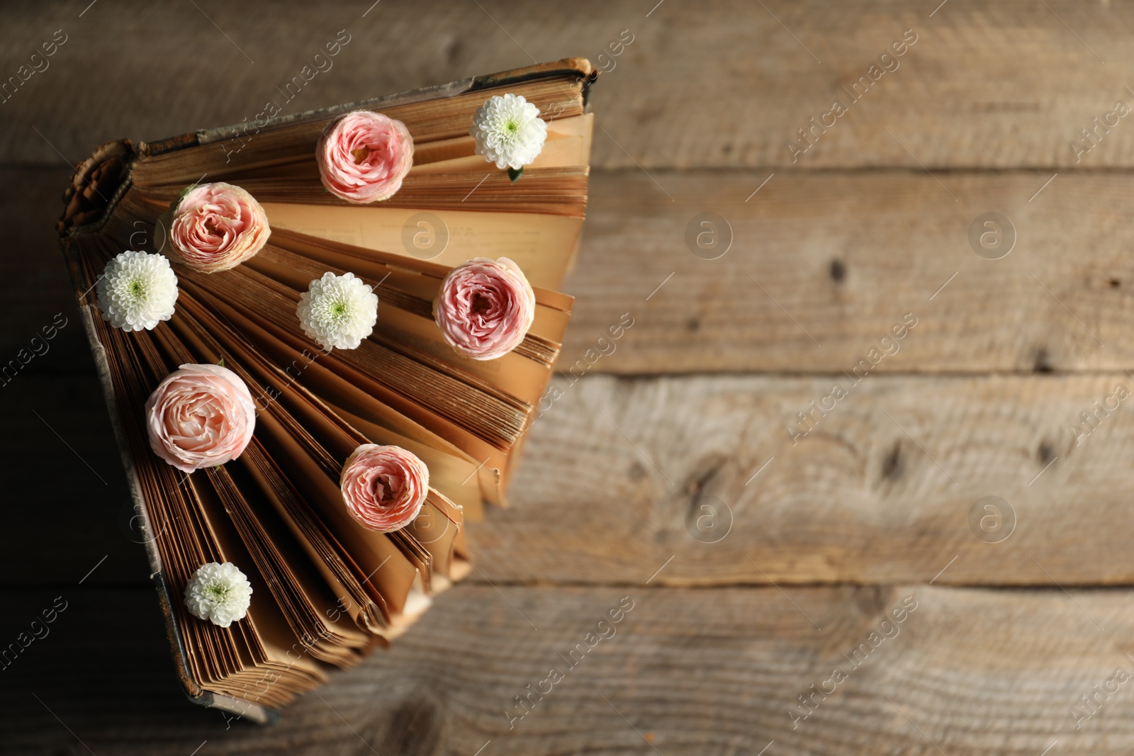 Photo of Book with beautiful flowers on wooden table, top view. Space for text