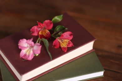 Photo of Books and beautiful flowers on wooden table, closeup