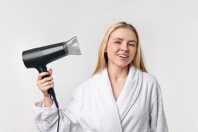 Photo of Beautiful young woman drying her hair with hairdryer on light grey background