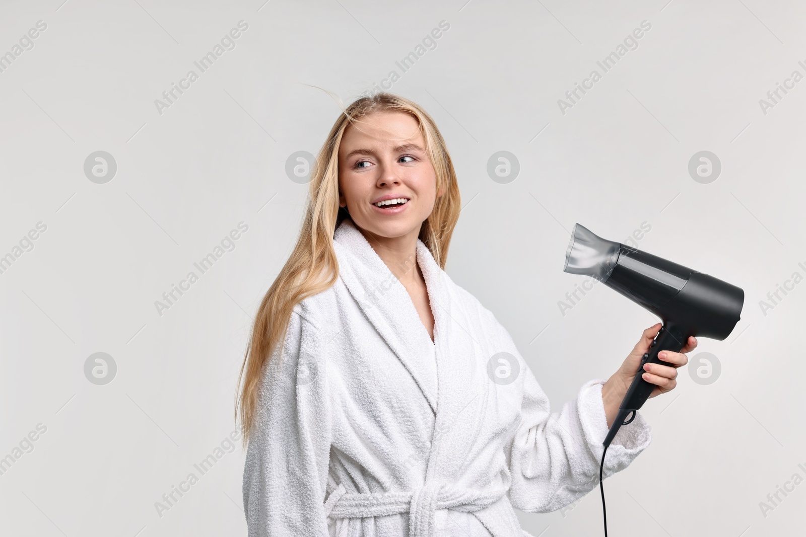 Photo of Beautiful young woman drying her hair with hairdryer on light grey background