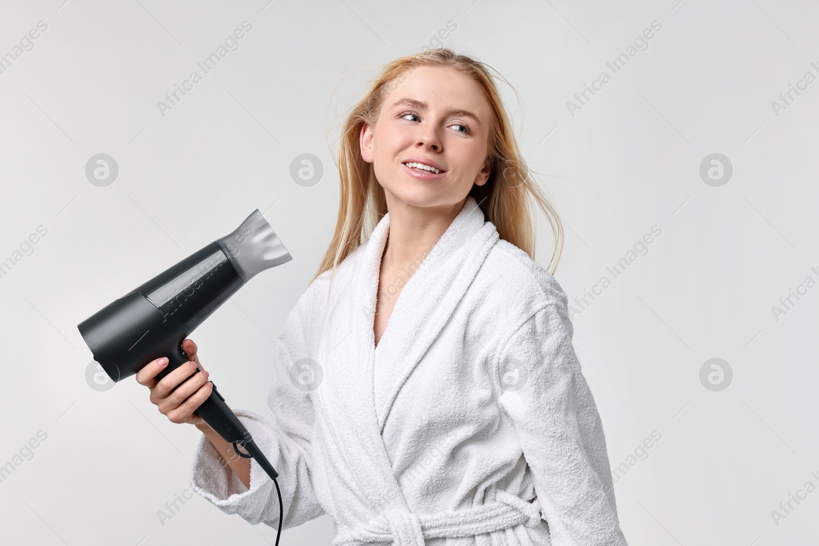 Photo of Beautiful young woman drying her hair with hairdryer on light grey background