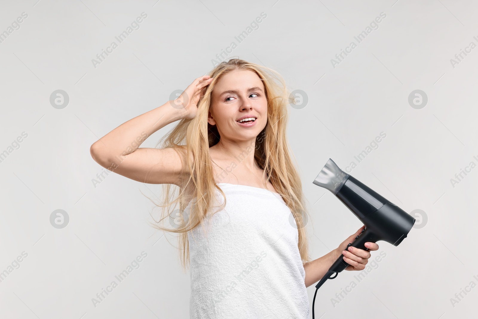 Photo of Beautiful young woman drying her hair with hairdryer on light grey background