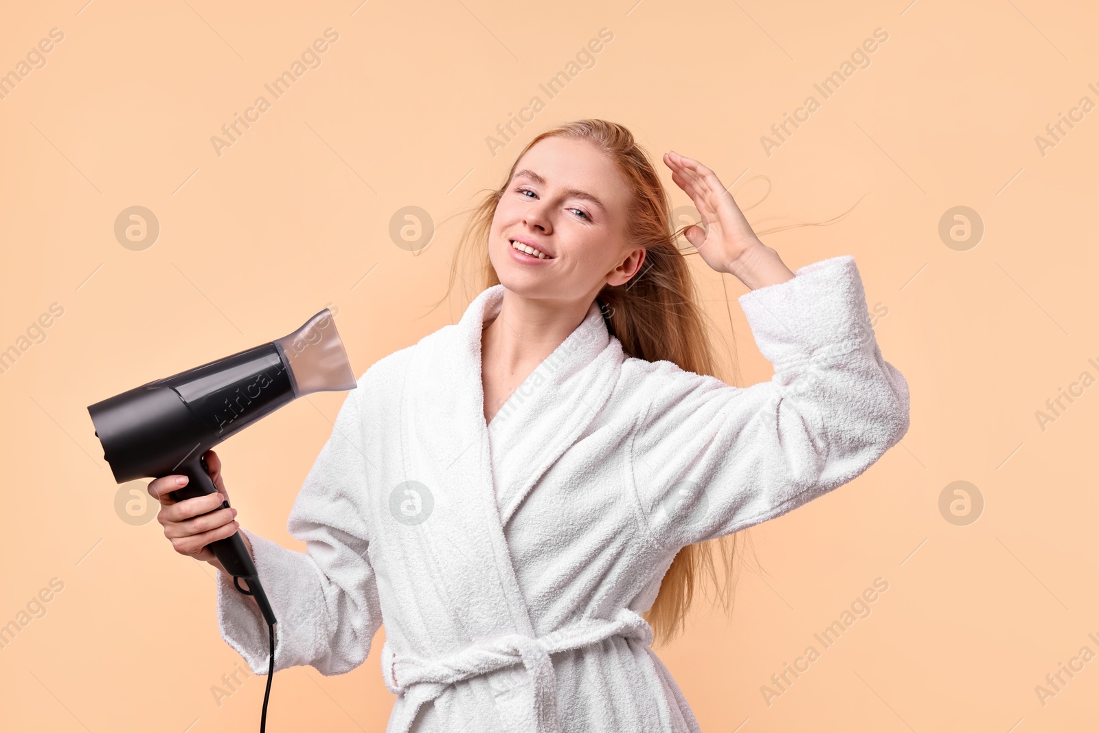 Photo of Beautiful young woman drying her hair with hairdryer on beige background