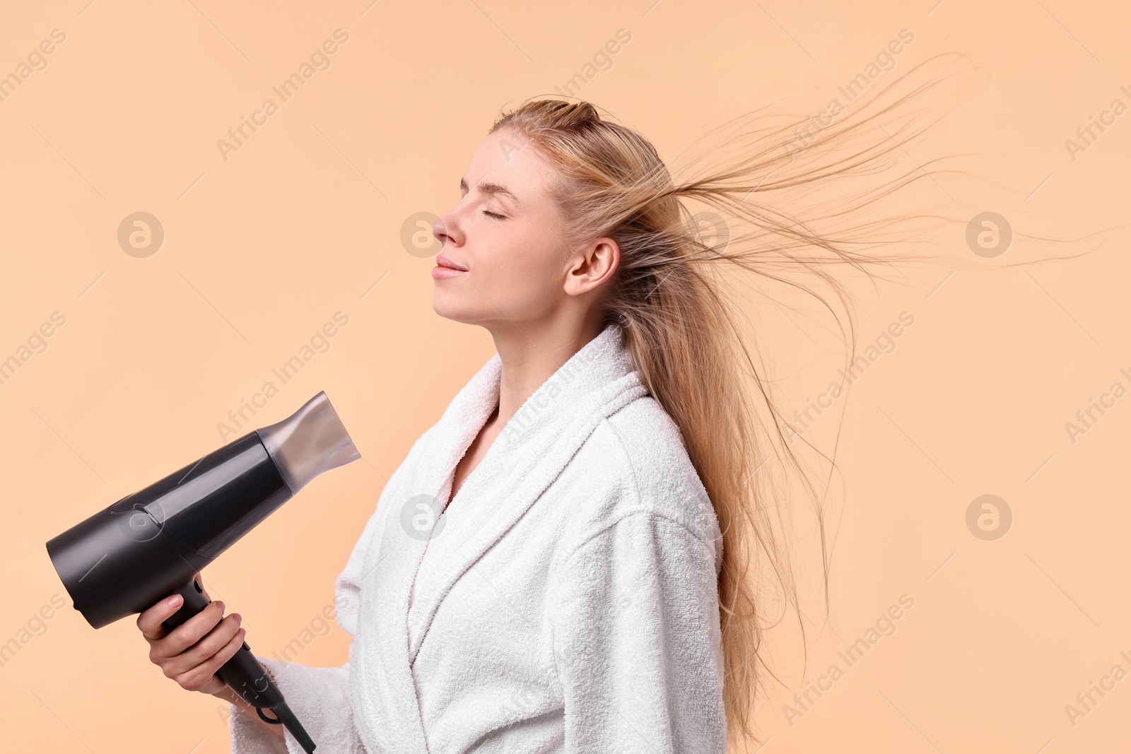 Photo of Beautiful young woman drying her hair with hairdryer on beige background