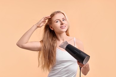 Photo of Beautiful young woman drying her hair with hairdryer on beige background