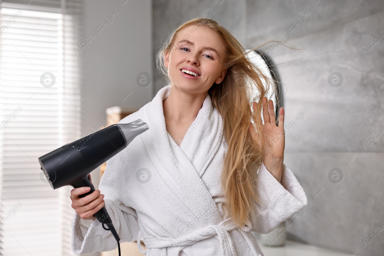 Photo of Beautiful young woman drying her hair in bathroom