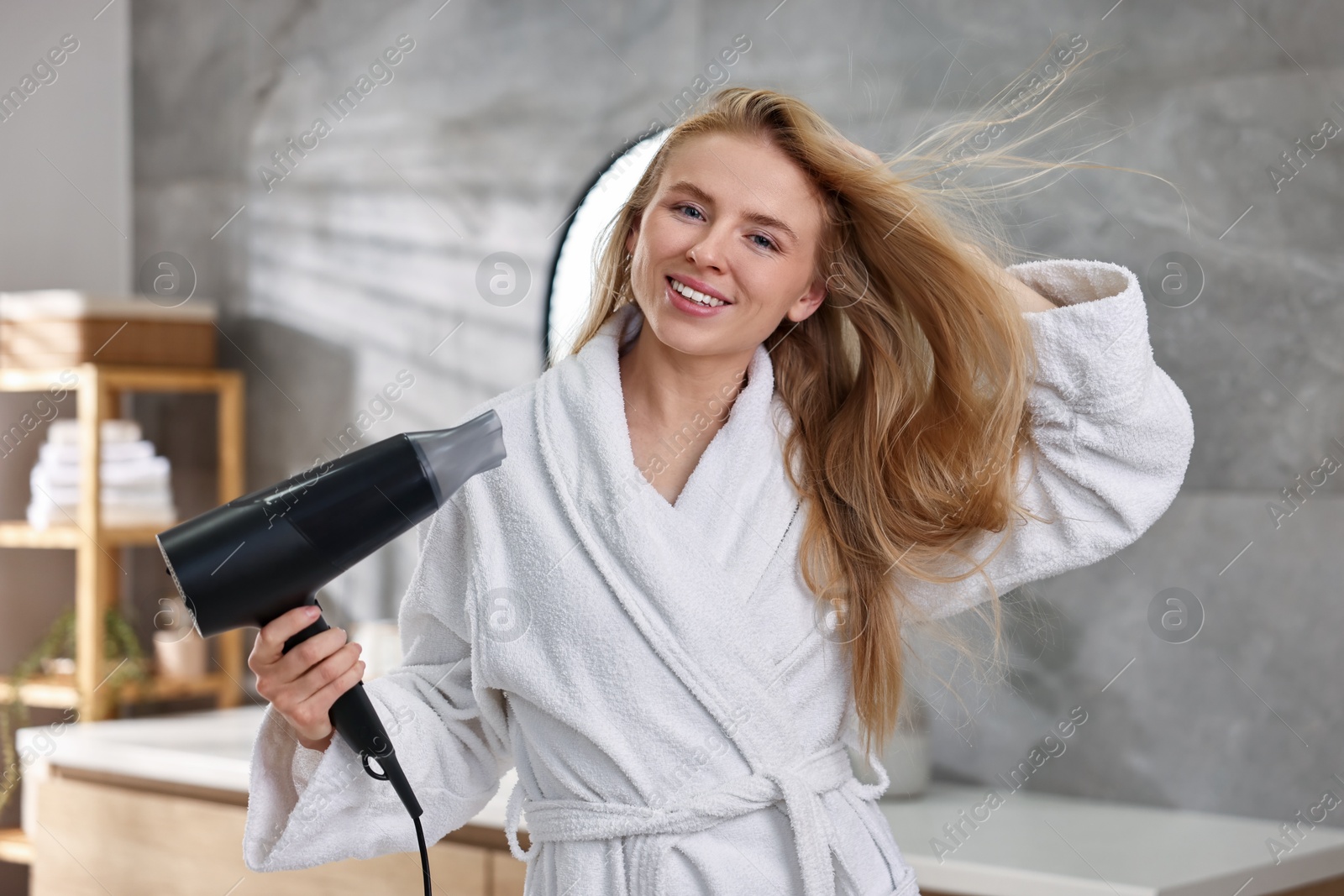 Photo of Beautiful young woman drying her hair in bathroom