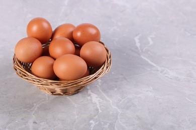 Photo of Wicker basket with fresh eggs on grey marble table, closeup. Space for text