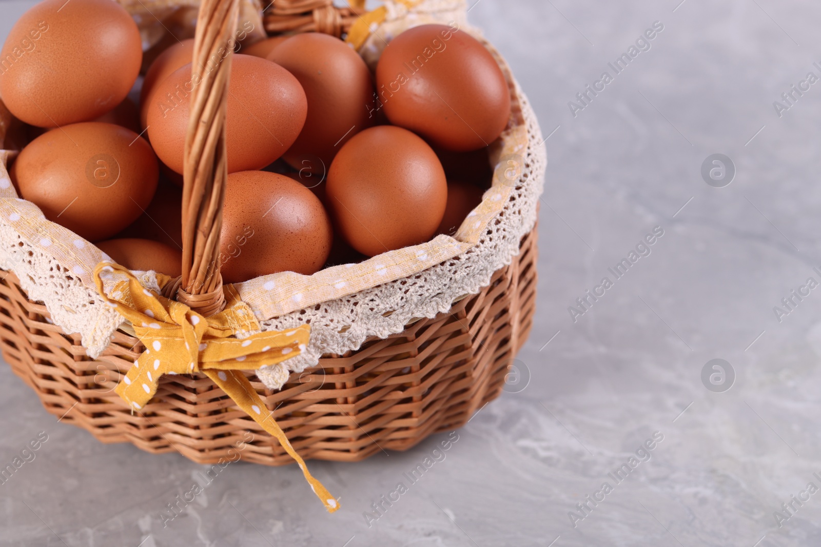 Photo of Wicker basket with fresh eggs on grey marble table, closeup. Space for text