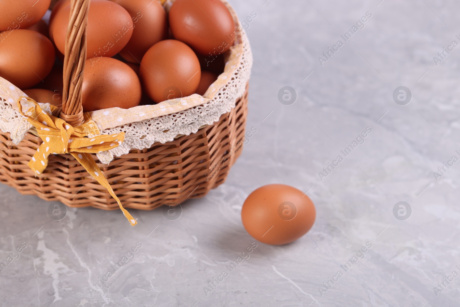 Photo of Wicker basket with fresh eggs on grey marble table, closeup. Space for text