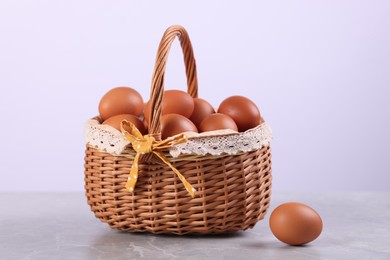 Photo of Wicker basket with fresh eggs on grey marble table against white background, closeup