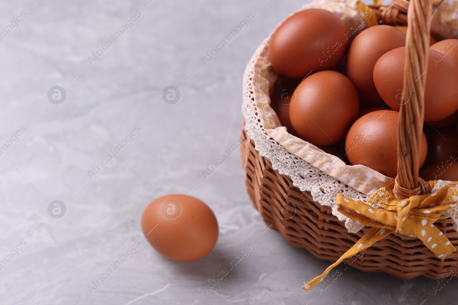 Photo of Wicker basket with fresh eggs on grey marble table, closeup. Space for text