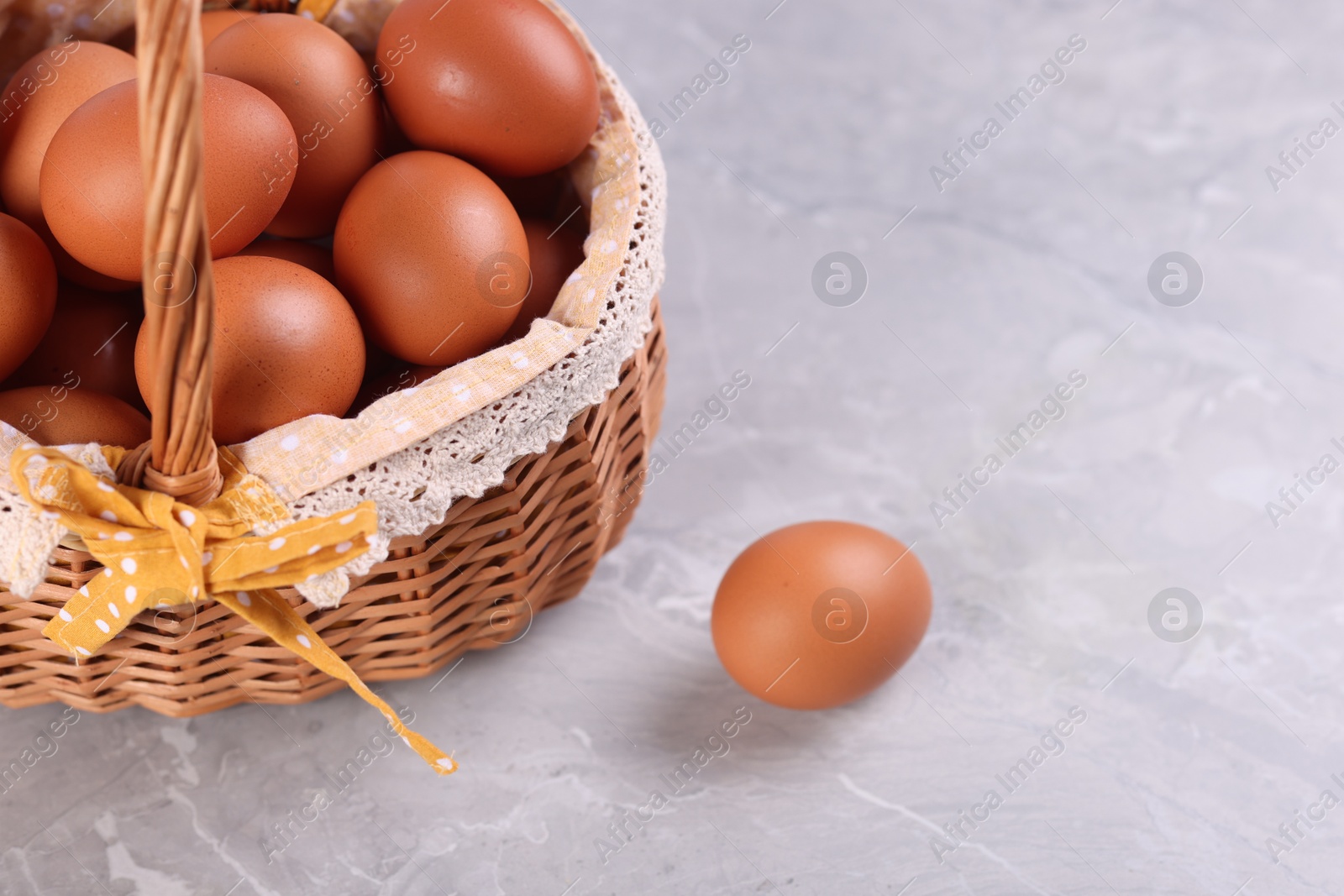 Photo of Wicker basket with fresh eggs on grey marble table, closeup. Space for text