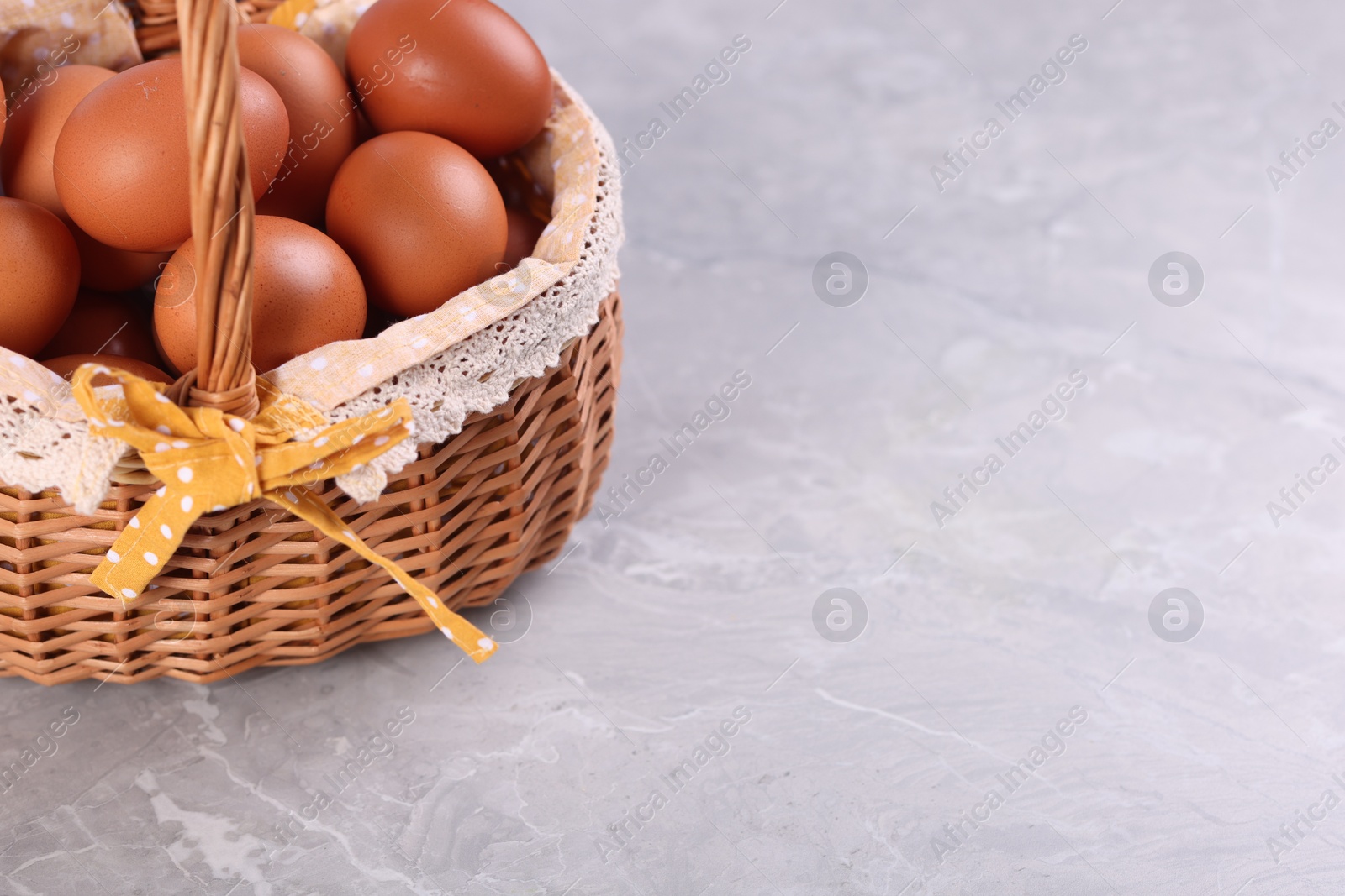 Photo of Wicker basket with fresh eggs on grey marble table, closeup. Space for text