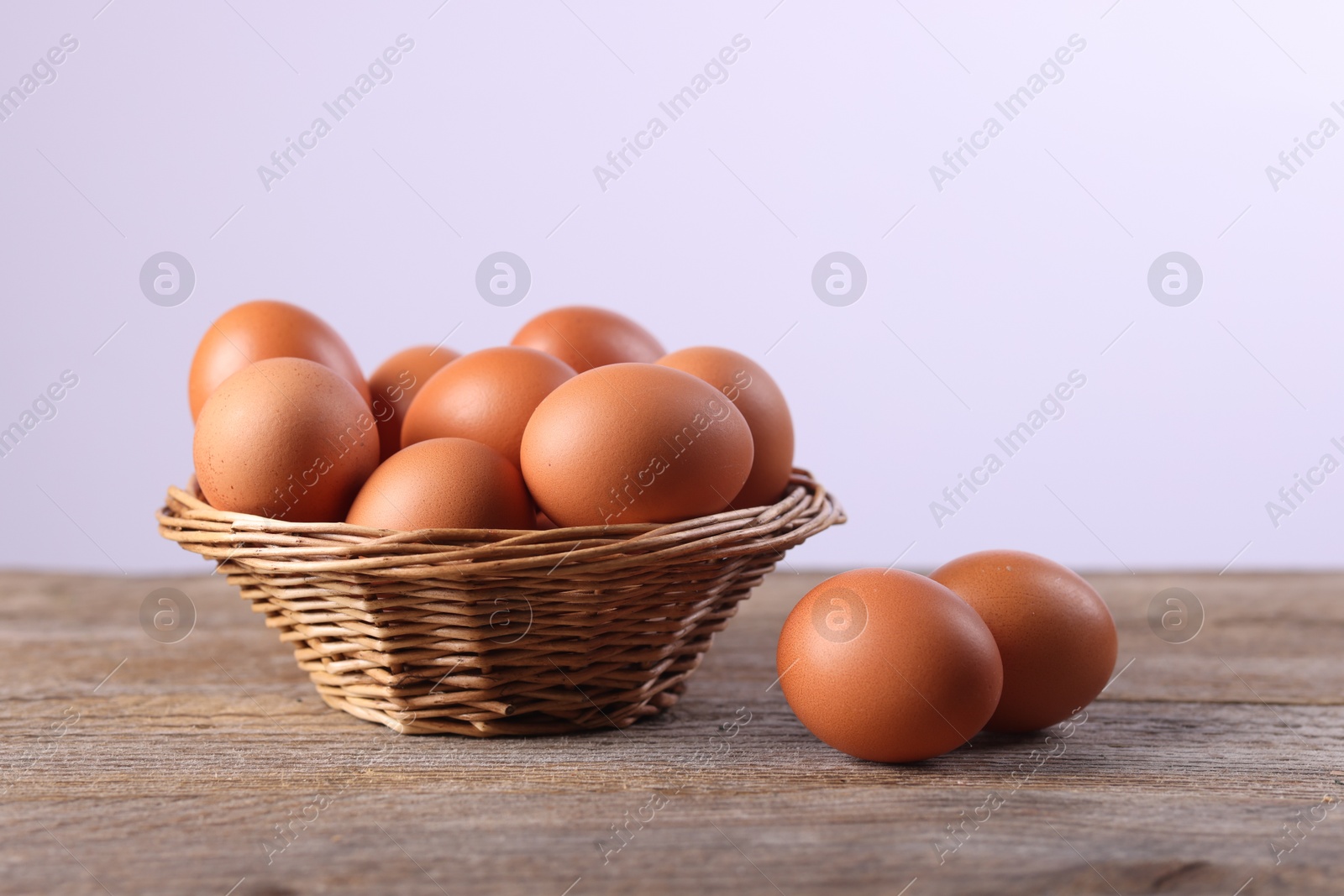 Photo of Wicker basket with fresh eggs on wooden table against white background, closeup