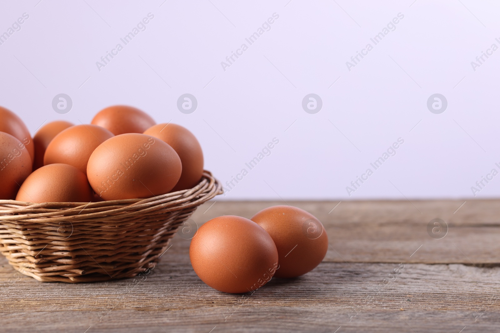 Photo of Wicker basket with fresh eggs on wooden table against white background, closeup. Space for text