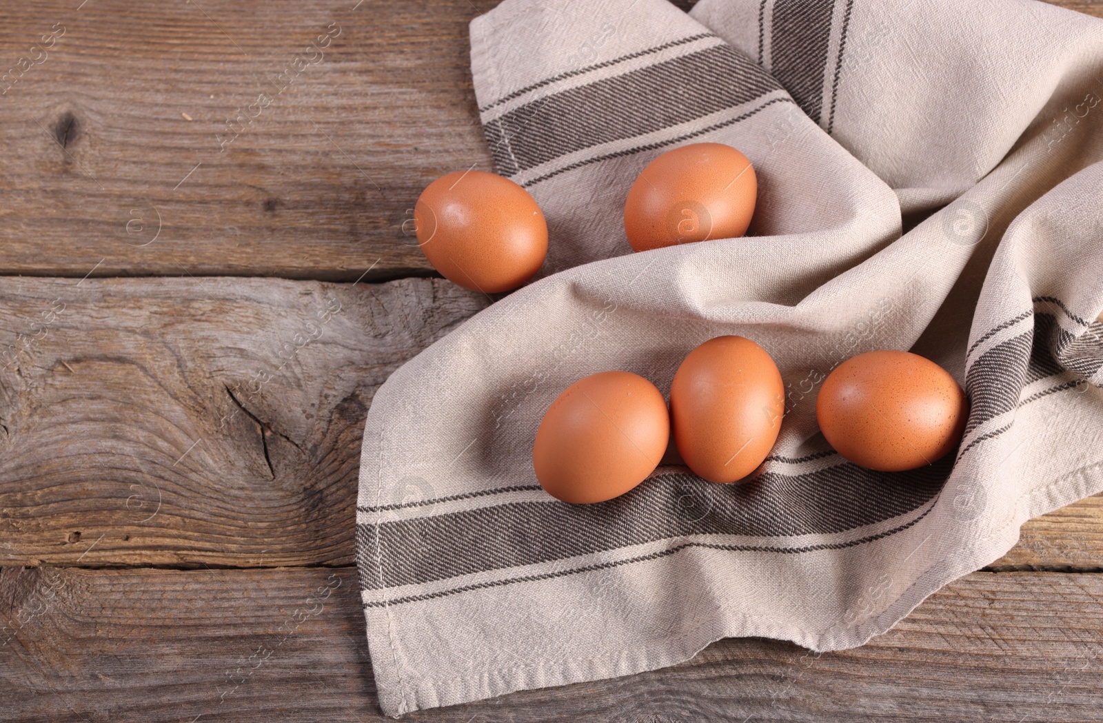 Photo of Many fresh eggs and towel on wooden table, flat lay. Space for text