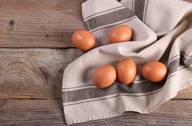 Photo of Many fresh eggs and towel on wooden table, flat lay. Space for text