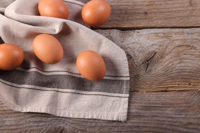 Photo of Many fresh eggs and towel on wooden table, flat lay. Space for text