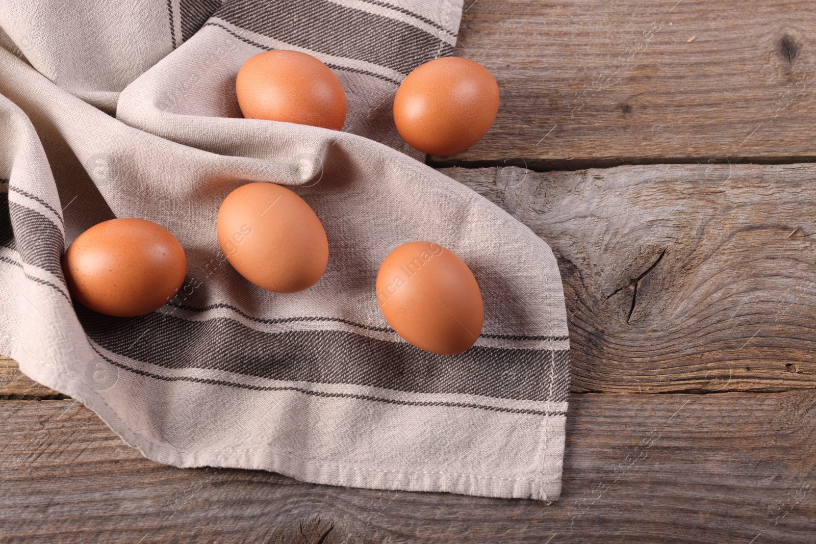 Photo of Many fresh eggs and towel on wooden table, flat lay. Space for text