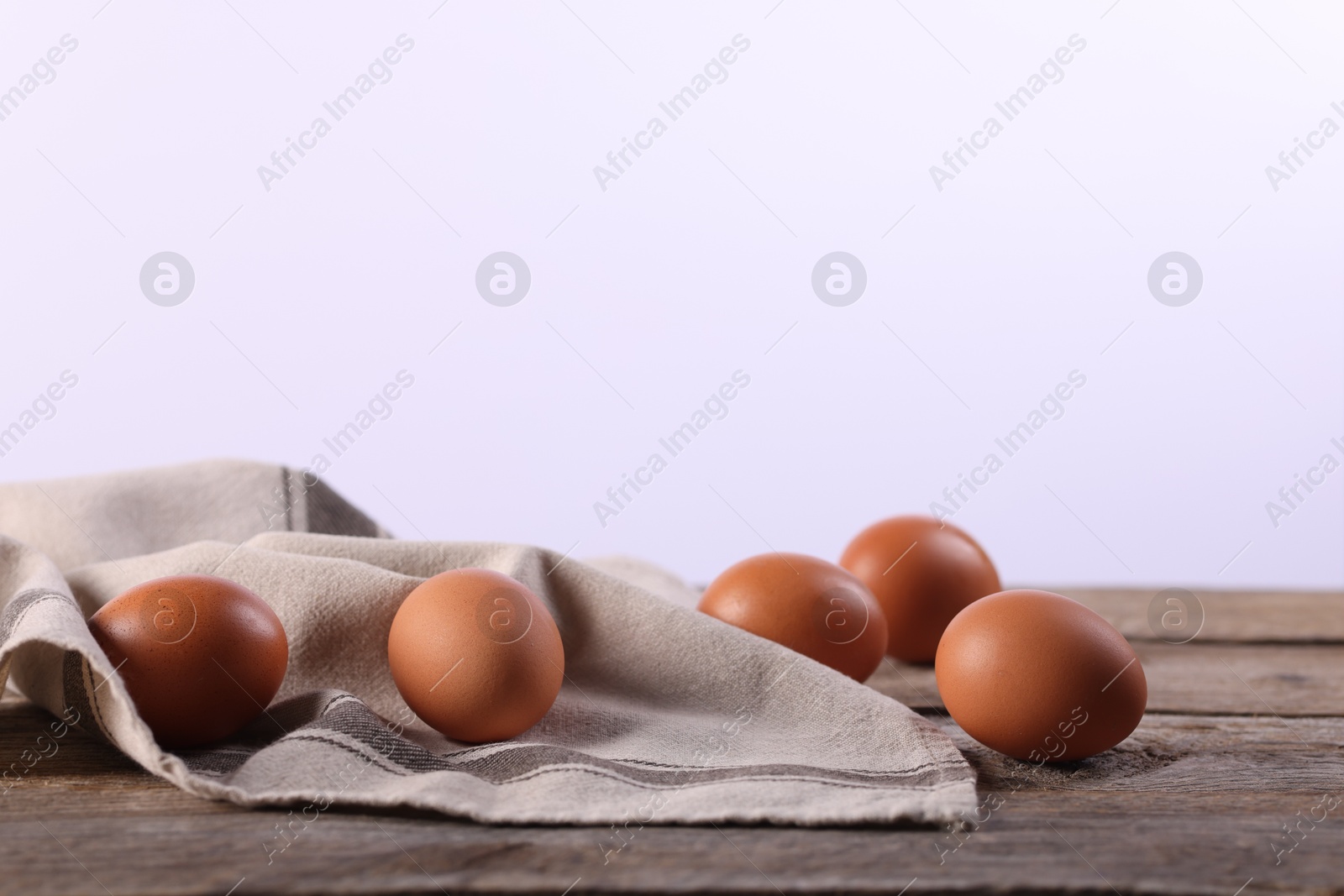 Photo of Many fresh eggs and napkin on wooden table against white background, closeup. Space for text