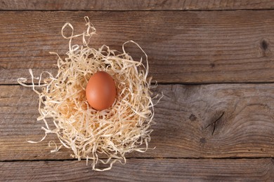 Photo of One fresh egg in nest on wooden table, top view. Space for text