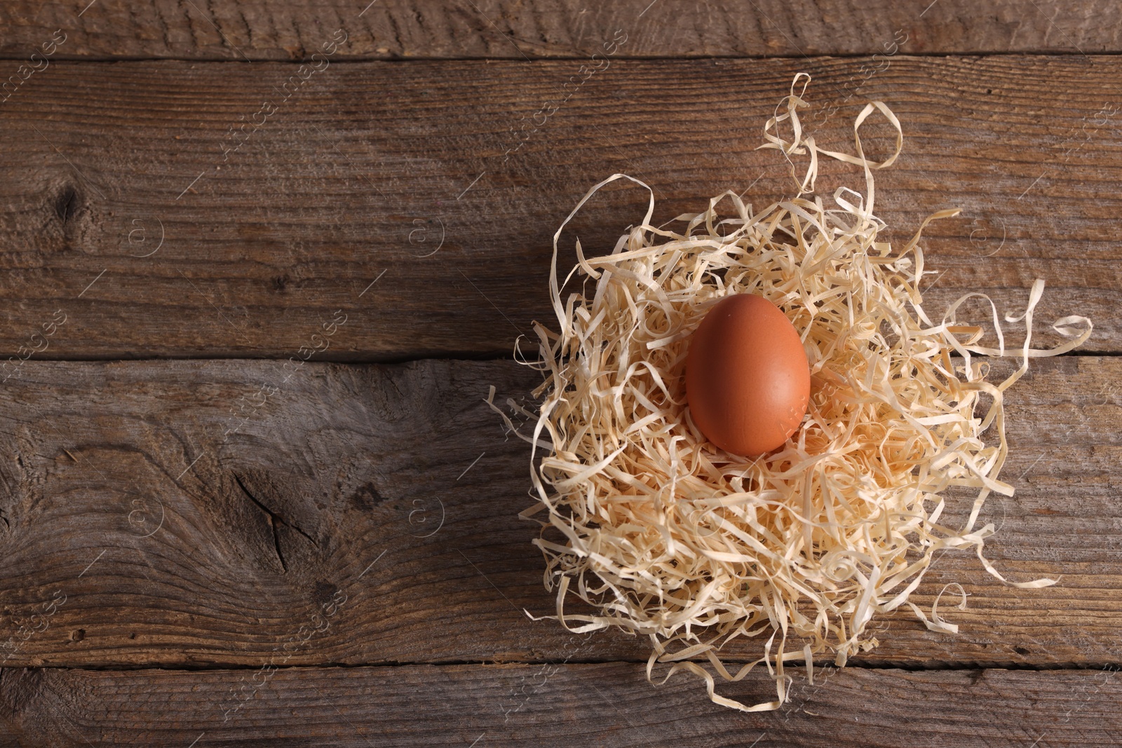 Photo of One fresh egg in nest on wooden table, top view. Space for text