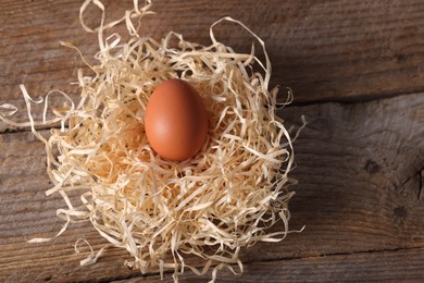 Photo of One fresh egg in nest on wooden table, above view