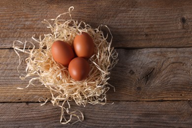 Photo of Fresh eggs in nest on wooden table, top view. Space for text