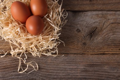 Photo of Fresh eggs in nest on wooden table, top view. Space for text