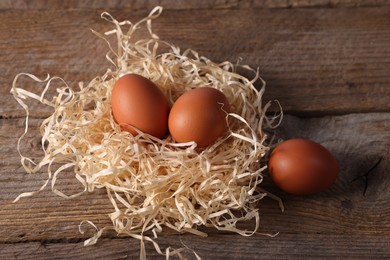 Photo of Fresh eggs in nest on wooden table, above view