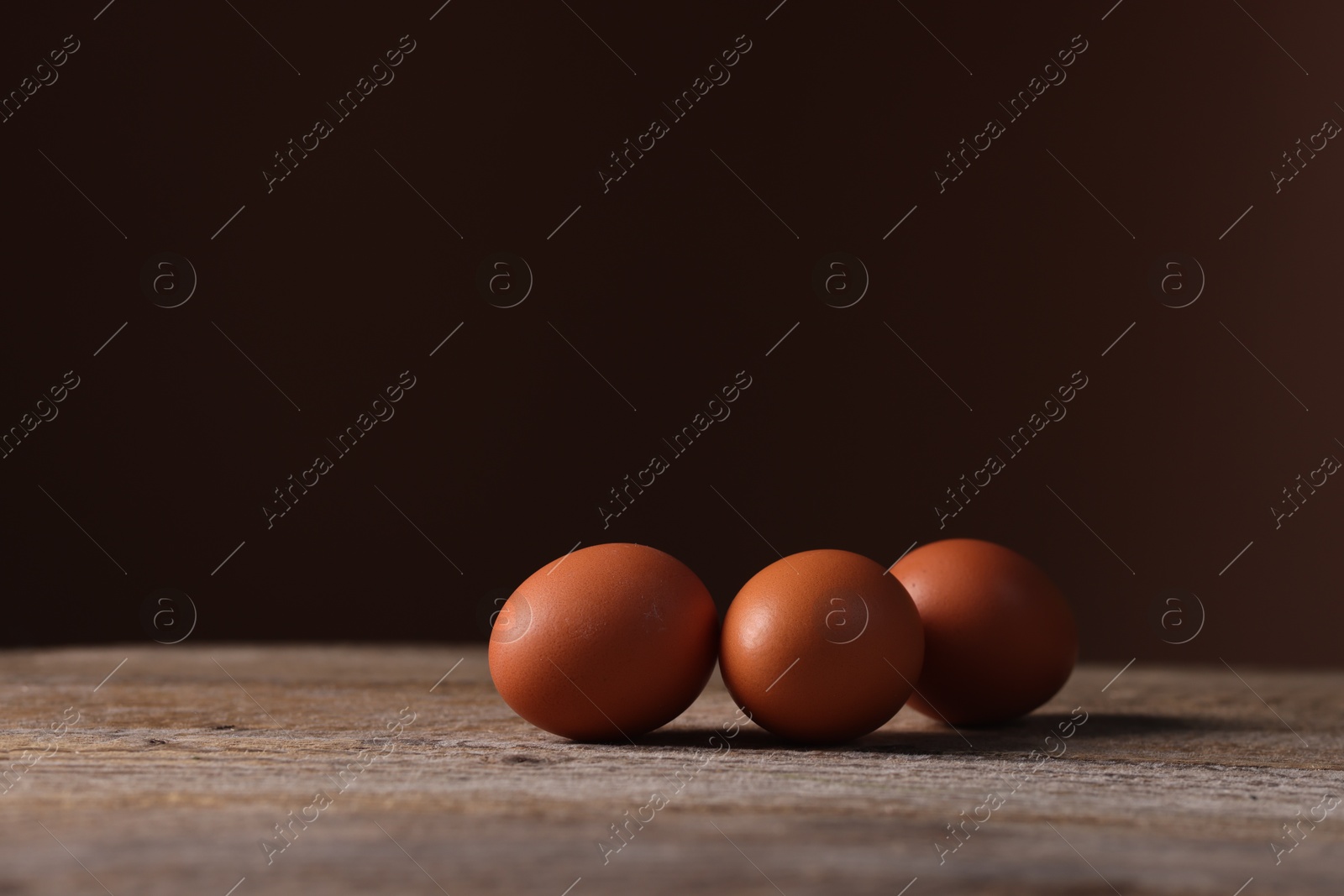 Photo of Fresh eggs on wooden table against brown background, closeup. Space for text