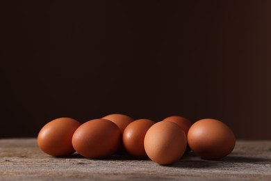 Photo of Fresh eggs on wooden table against brown background, closeup. Space for text