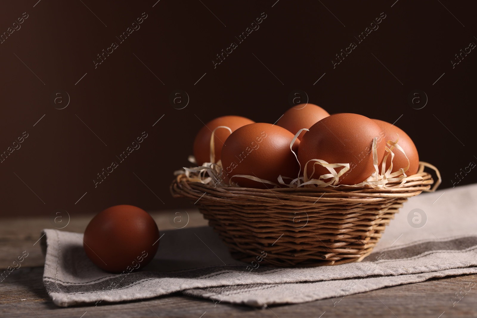 Photo of Wicker basket with fresh eggs on wooden table against brown background, closeup