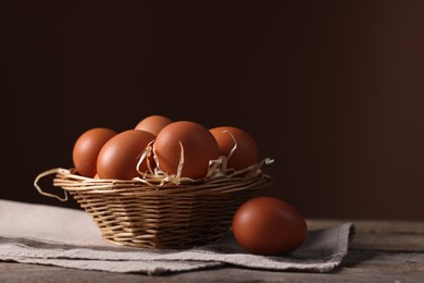 Photo of Wicker basket with fresh eggs on wooden table against brown background, closeup