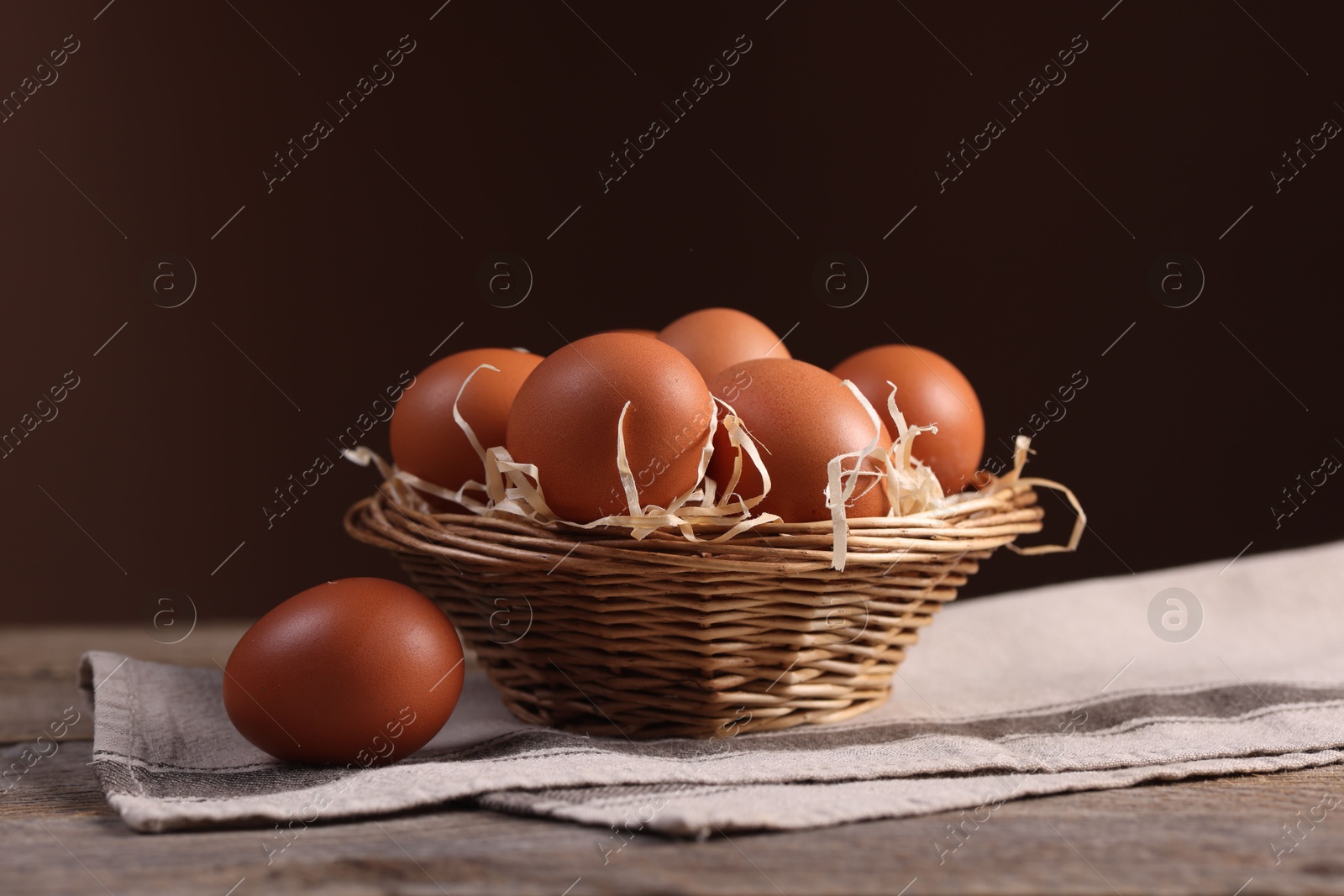 Photo of Wicker basket with fresh eggs on wooden table against brown background, closeup