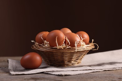 Photo of Wicker basket with fresh eggs on wooden table against brown background, closeup