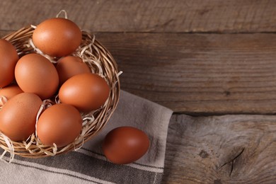 Photo of Wicker basket with fresh eggs on wooden table, top view. Space for text