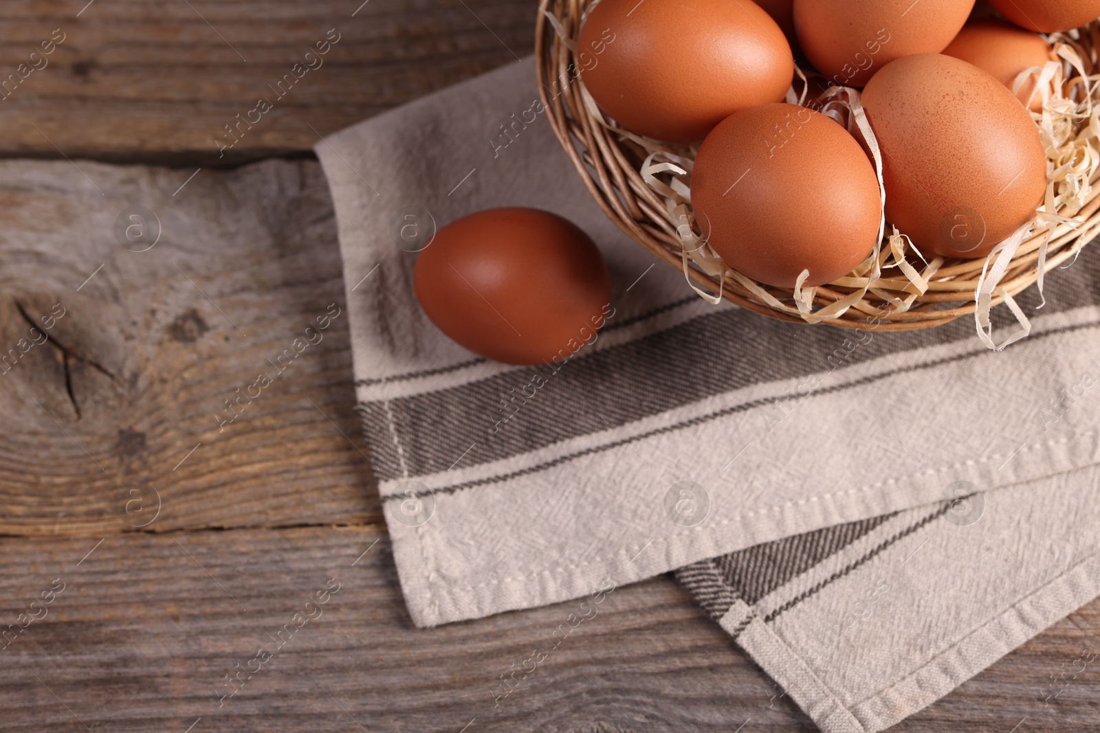 Photo of Wicker basket with fresh eggs on wooden table, top view. Space for text